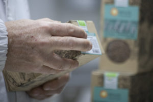 Close-up van een hand die een verpakte doos graan vasthoudt, verzegeld met een Bioles-productetiket