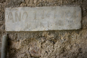 A handmade sign attached to a wall, reading Anno 1961 by, then followed by a series of initials