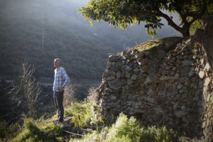 Jose González de pie junto a la pared de una terraza de piedra a la luz del sol, mirando a través de un valle