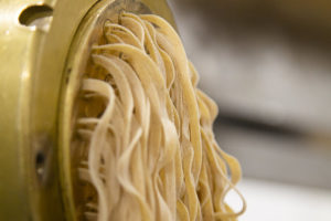 Fresh tagliatelle being pressed through a pasta machine
