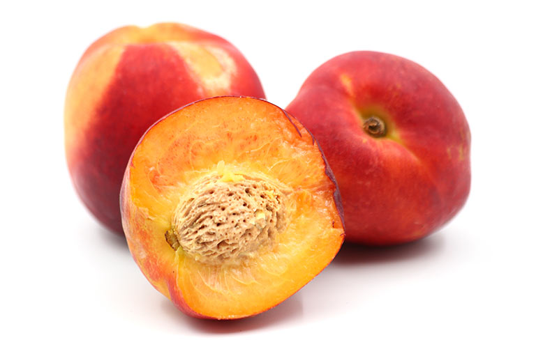 A group of three nectarines, one of them cut in half to show the orange flesh and stone inside