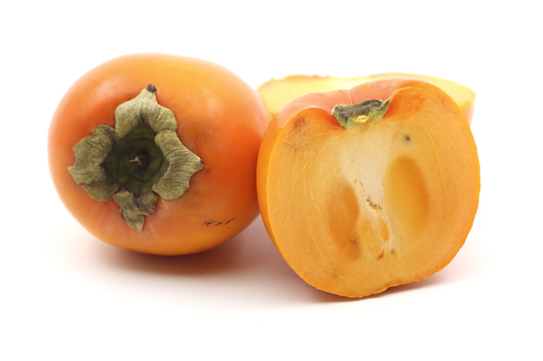 Two Sharon fruit, one cut open to show the orange flesh inside