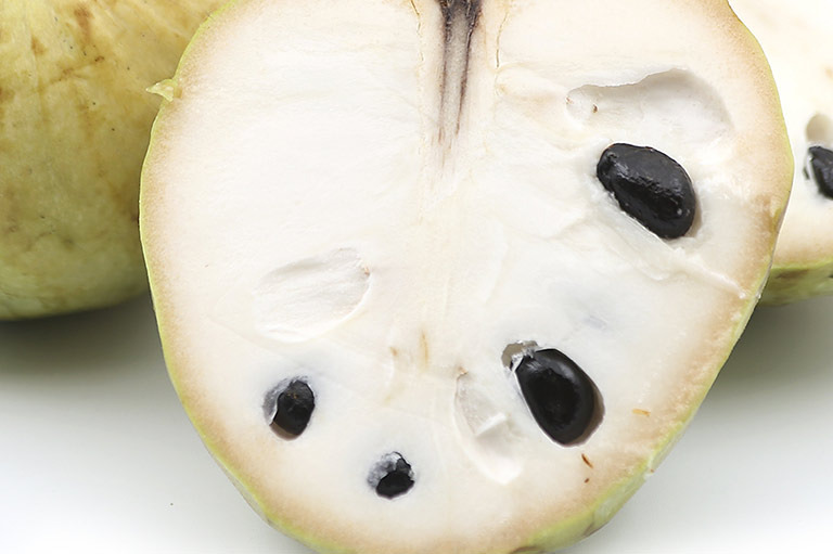 Close-up van een gesneden custardappel, met het witte vruchtvlees en de zwarte zaden erin