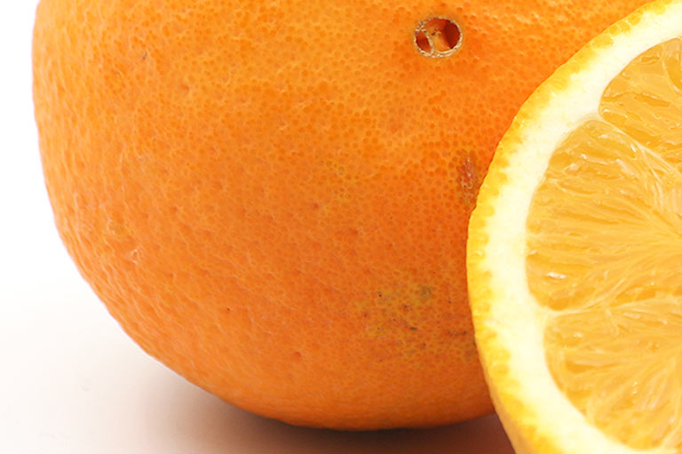 Close-up van de schil van een Navelina-sinaasappel, waarbij het bloesemuiteinde zichtbaar is dat lijkt op een menselijke navel