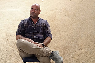 Organic farmer Jose Daniel Carbonell sitting in his warehouse, a tall hill of harvested rice behind him