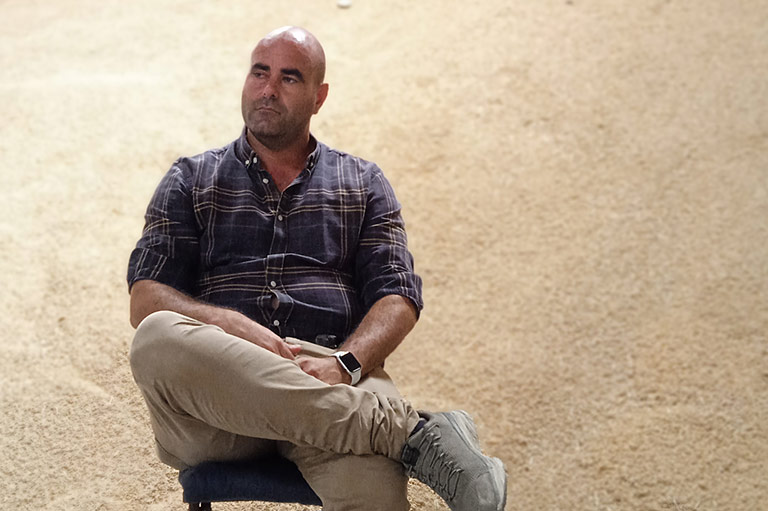 El agricultor orgánico José Daniel Carbonell sentado en su almacén, con una alta colina de arroz cosechado detrás de él