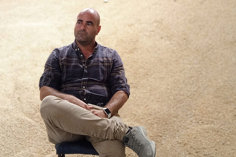 Organic farmer Jose Daniel Carbonell sitting in his warehouse, a tall hill of harvested rice behind him