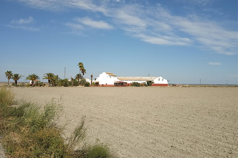 Een wit pakhuis omringd door geploegde velden